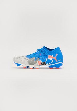 Chaussure de football bleue et grise avec des crampons orange, des lacets et un logo Puma, avec des motifs graphiques et le texte « FOREVER » sur le talon.
