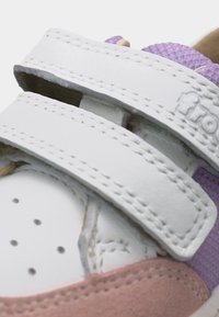 Κοντινό πλάνο ενός αθλητικού παπουτσιού με λευκές διπλές λουρίδες βέλκρο, μωβ υφασμάτινη υφή και ροζ σουέντ λεπτομέρειες.