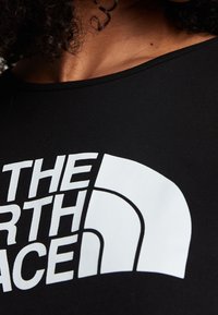 Camiseta negra con un gran logo en blanco que dice "THE NORTH FACE." La tela parece suave con un escote ajustado.