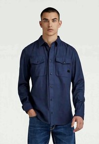 Camisa azul marino de botones en mezcla de algodón, con dos bolsillos en el pecho, cierres de botones y un diseño de cuello clásico. Tejido texturizado con un ligero brillo.