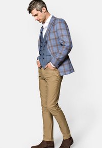 Niebieska kratkowana marynarka na niebieską kamizelkę, biała koszula i beżowe chinosy. Ciemnobrązowe botki do kostki dopełniają outfit, który ma dopasowany krój i gładki materiał.