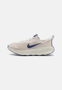 Zapatilla de running Nike en tono beige claro con el logo swoosh azul, suela blanca gruesa y detalles azules en el borde de la suela y en el lazo del talón.
