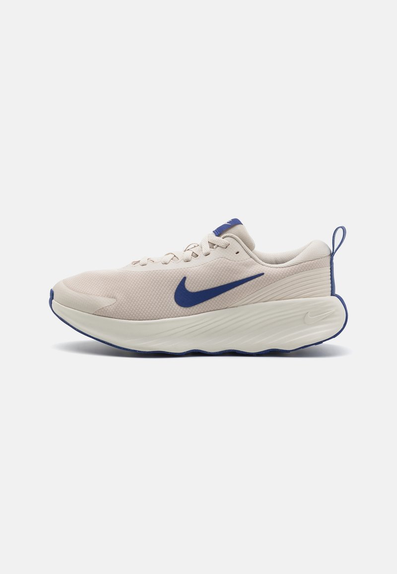 Zapatilla de running Nike en tono beige claro con el logo swoosh azul, suela blanca gruesa y detalles azules en el borde de la suela y en el lazo del talón.