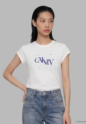 Ung kvinde med glat sort hår iført en hvid Calvin Jeans t-shirt og blå denimjeans, stående med den ene hånd på hoften.