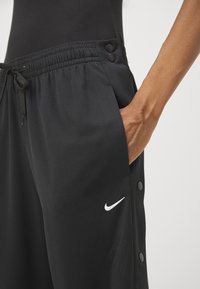 Melni sporta bikses ar struktūrētu apdari, elastīgu jostasvītru, auklu, sānu kabatām un baltu Nike logotipu. Plastmasas pogas sānos.