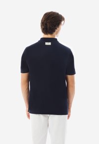 Navyblaues Poloshirt mit kurzen Ärmeln, ausgestattet mit einem klassischen Kragen und einem kleinen Markenetikett auf der Rückseite. Glatte Textur, leicht taillierter Schnitt.