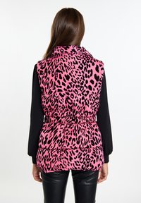 Rosa Leopard-Print Steppweste, tailliert mit hohem Kragen. Schwarzes Langarmshirt darunter sichtbar. Strukturierter Stoff.