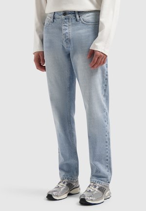 Person wearing light blue straight-leg jeans, white long-sleeve shirt, and silver-gray athletic shoes on plain background.