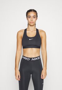 Black sports bra with a scoop neckline and white Nike logo, paired with high-waisted black leggings featuring a bold white "PRO NIKE" waistband.