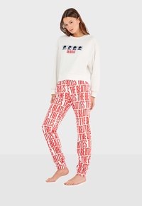 Sudadera blanca con gráfico de "The Beatles" y pantalones de pijama rojos con un patrón que presenta texto repetido de "The Beatles" en negrita.