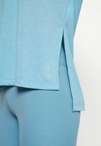 Närbild av en person som bär ljusblå träningsleggings och en matchande lös topp med sidslitsar och en liten Nike-logga.