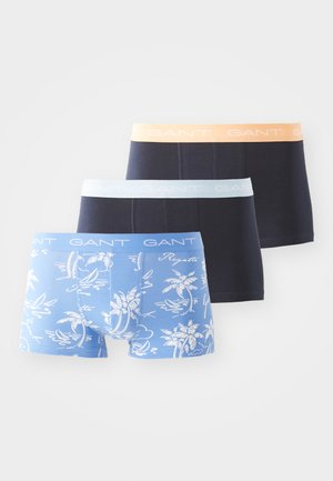 Três pares de boxers GANT: um em azul claro com padrão de palmeiras, um em azul escuro e um em preto sólido, cada um com cores de cintura contrastantes.