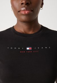 Černé bavlněné tričko s nápisem "TOMMY JEANS" a "NEW YORK CITY" v bílé a červené barvě, s malým logem ve středu. Kulatý výstřih.