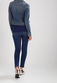 Kort denimjacka i ljusblått, figursydd design, matchad med en marinblå topp, mörkblå skinny jeans och sneakers i svart och rosa. Fransade fållar.