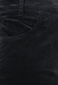 Schwarzer Denim-Stoff mit einer glatten Textur, ausgestattet mit einer Seitentasche und einem dezenten Glanz. Die Nähte sind in einer kontrastierenden Farbe für zusätzlichen Detailreichtum.