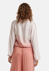 Seidenbluse, die von Weiß zu sanftem Pfirsich übergeht, mit langen Ärmeln und lockerer Passform, kombiniert mit plissierten, hellrosa Hosen.