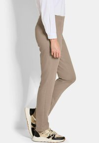 Lichtbeige op maat gemaakte broek met een gladde textuur, gecombineerd met zwart en beige sneakers. Het shirt is wit met lange mouwen.