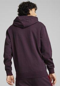 Kapuzensweatshirt aus dunkelpurpurfarbenem Baumwollmaterial mit einer lockeren Passform, gerippten Bündchen und einem kontrastierenden roten Akzent am Saum.
