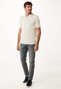 Biała koszulka polo z krótkim rękawem, z kołnierzykiem i dwoma czarnymi guzikami, zestawiona z szarymi dżinsami i czarnymi trampkami. Gładka tekstura, dopasowany krój.