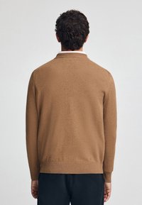 Brauner Strickpullover mit einem lässigen Design, das lange Ärmel und einen gerippten Saum aufweist. Das Material wirkt weich und hat eine subtile Textur.
