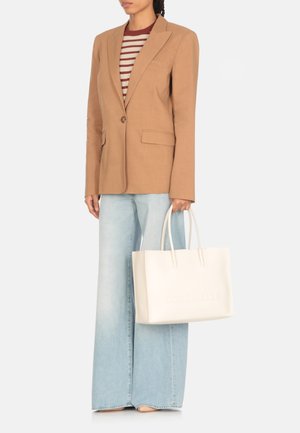 Blazer beige su misura, top a righe bordeaux e bianche, jeans a gamba larga azzurri chiari e borsa in pelle bianca con logo in rilievo "COCCINELLE".