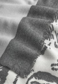 Écharpe grise et blanche à motifs, avec une finition douce et texturée, des bords effilochés et un motif géométrique subtil dans le tissu.
