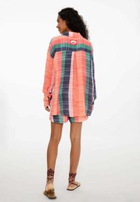 Pestrý pruhovaný dlhý rukáv, oranžový, ružový, zelený, námornícky; obsahuje zadný rozparok a detail loga. Spárovaný s ladiacimi šortkami.