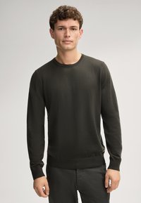 Dunkelgrüner Langarmpullover mit Rundhalsausschnitt, gerippten Bündchen und glatter Textur. Figurbetontes Design, minimalistisch ohne Muster oder Akzente.