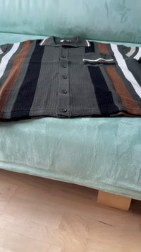 Cămașă tricotată cu nasturi, cu dungi negre, maronii și albe, având un buzunar pe partea stângă și guler și manșete cu nervuri.