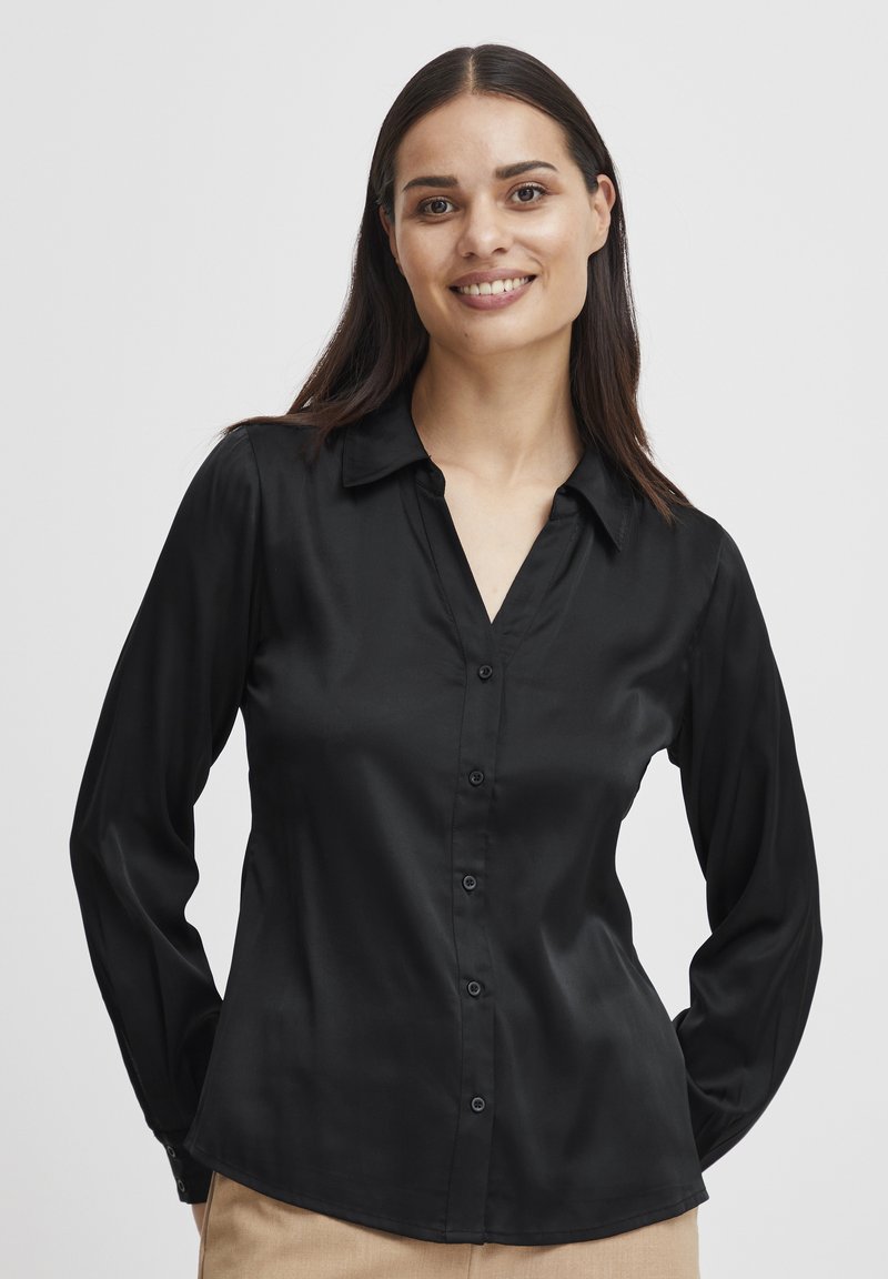 Schwarzes Satin-Hemd mit langen Ärmeln, Knopfleiste, Kragen und tailliertem Design. Glatte Textur mit subtiler glänzender Optik. Strukturiertes Silhouette.