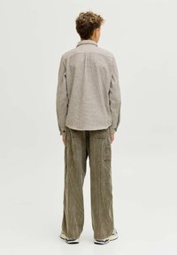 Camicia grigia a fantasia con colletto e polsini abbottonati; abbinata a pantaloni a gamba larga in velluto verde e sneakers. Design semplice con una trama tessile.