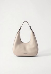 Sac à bandoulière en cuir crème avec une forme incurvée et une seule anse noire, doté d'un petit logo de marque métallique sur le devant.