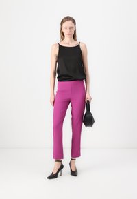 Top en satin noir, pantalon tailleur rose vif, chaussures à talons hauts noires, sac à main noir, texture lisse, design minimaliste, silhouette ajustée.