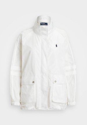 Biała nylonowa kurtka z wysokim kołnierzem, dwiema przednimi kieszeniami i elastycznymi mankietami. Posiada małe niebieskie logo na lewej piersi oraz paskowane akcenty.