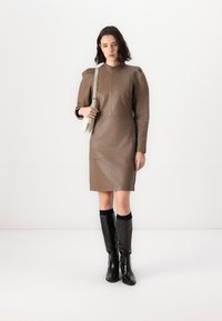 Rochie din piele maro cu umeri structurați, silueta ajustată și mâneci lungi. Purtați cu cizme negre până la genunchi și o geantă ușoară.