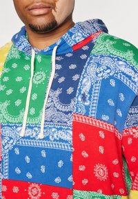 Kolorowa bluza z kapturem z motywem patchworkowym w kolorach czerwonym, niebieskim, zielonym, żółtym z wzorem paisley. Materiał to mieszanka bawełny z sznurkami.