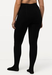 Leggings neri con una texture a coste, vita alta e vestibilità a lunghezza intera, mostrati da dietro con i piedi nudi su uno sfondo neutro.