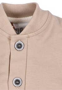 Beżowa koszula zapinana na guziki, z prążkowanym kołnierzykiem, dwoma srebrnymi guzikami i miękką, gładką fakturą materiału.