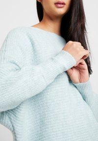 Hellblauer Strickpullover mit strukturiertem Muster, breiten Rippbündchen und lässiger Passform. Weiches, fluffiges Material sorgt für Komfort.