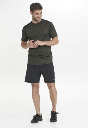 Olivgrön kortärmad sporttröja med rund hals, kombinerad med svarta shorts, båda tillverkade av lättviktsmaterial. Svarta sportskor.