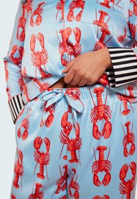 Satängpyjamasuppsättning med blå bakgrund och upprepande röd hummerdesign. Försedd med svarta och vita randiga manschetter.