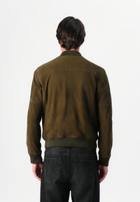 Ελαιόχρωμο σουέτ μπόμπερ τζάκετ με ραμμένα μανίκια και στρίφωμα, με απαλό υφή και ραφές στην πλάτη για δομή.