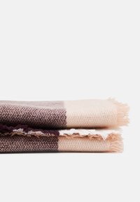 Couverture en mélange de laine tissée dans des teintes de rose et de violet foncé, avec des franges. Pliée soigneusement, mettant en avant des motifs géométriques et des couleurs contrastées.