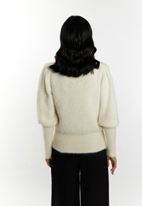 Crèmekleurige trui met een pluizige textuur, opgeblazen mouwen en een strakke geribbelde tailleband; gecombineerd met zwarte wijde broek.