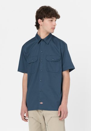 Camicia a maniche corte con bottoni in tessuto blu scuro, dotata di due tasche sul petto, colletto a punta e un piccolo cartellino con logo sull'orlo.
