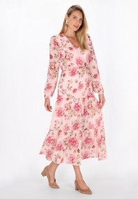 Rochie florală roz cu mâneci lungi, decolteu în V și fustă în straturi. Conține un material ușor, transparent, cu o textură moale și un model floral.