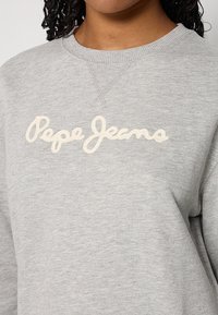 Sudadera gris hecha de tela suave con cuello redondo, con el logo "Pepe Jeans" en cursiva beige en el pecho.