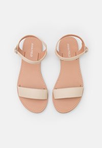 Beige tasapohjaiset sandaalit, joissa on kaksi leveää hihnaa ja nilkkasolki. Sileä materiaali ja pehmustettu pohja. Hieman muotoiltu, kevyt design.
