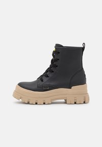 Bottines en cuir synthétique noir avec une semelle beige épaisse, bout rond, six oeillets et une languette au talon. Surface texturée et design durable.