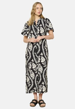 Schwarz-weiß gemustertes Midikleid mit kurzen Ärmeln, Blattdesign, Knopfverschluss vorne und lockerer Passform; kombiniert mit schwarzen Sandalen.